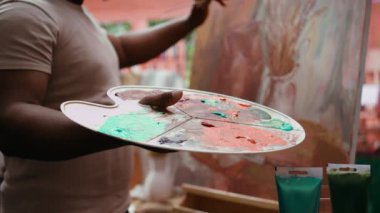 Kendine güvenen ressam palette farklı suluboyaları karıştırarak mükemmel gölgeyi yaratıyor ve güzel sanatlara, tuvale uyguluyor. Sanatçı canlı renkler ve dinamik fırça darbeleri kullanır. Kapatın. Kamera B.
