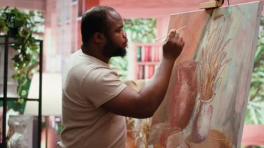 Güzel sanatlar atölyesinde yarattığı sanat eseri için suluboya boya boya kullanan ve paletteki renkleri karıştıran Afrikalı Amerikalı sanatçı. Tuvale kırsal öğeler çizen adam, yaratıcı süreç. Kamera A.