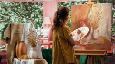 Güzel sanatlar atölyesinde yarattığı sanat eseri için suluboya boya boya kullanan ve paletteki renkleri karıştıran kadın ressam. Tuvale kırsal öğeler çizen bir kadın, atölyede yaratıcı bir süreç. Kamera A.