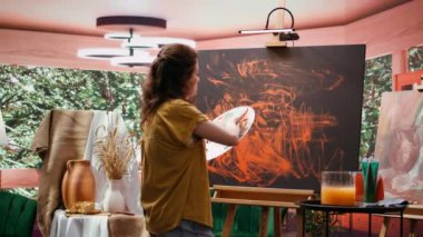 Ressam, son sanat eserinde parmak boyama tekniğiyle çalışır. Çağdaş sanat stüdyosu yaratıcılıkla uğuldar. Sanatçı canlı renkler ve modern boya tasarımı kullanır. Kamera B.