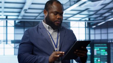 Bilgi işlem teknisyeni veri merkezinde yürüyor, tablet kullanarak sunucu işlemlerini denetliyor. Dijital aygıt, kamera A kullanılarak sunucu merkezinde optimal performans ve veri bütünlüğü sağlama uzmanı
