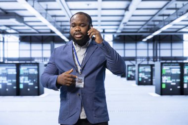 Yüksek teknoloji veri merkezinde gelişmiş bilgisayar ekipmanlarını barındıran bir iş adamı telefonda konuşuyor. Afrika kökenli Amerikalı bir adam telefon görüşmeleri sırasında teknolojik olarak gelişmiş bir çevrede görev veriyor.
