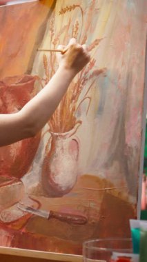 Sanat atölyesindeki modern boya fırçalarını kullanarak tuvale bir başyapıt çizmek için doğal kırsal unsurlardan esinlenilmiş dikey Video Sanatçısı. Sanat yaratıcılığı için motivasyon ve yaratıcılıkla çalışmak