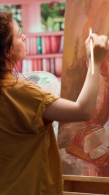 Dikey Video Becerikli ressam, suluboya bir kırsal sanat eserini resmeden bir tuvalin önünde duruyor. Sanatçı, boyaları karıştırıp çok renkli bir başyapıt yaratırken yeteneğini ve fırça tekniğini gösteriyor. Kamera.