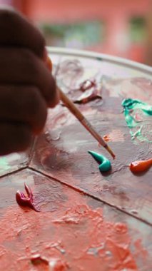 Modern araçları ve resim malzemelerini kullanarak bir sanat eseri oluşturan Dikey Video Yetenekli Sanatçı, yaratıcı süreci sırasında bir palette suluboya karıştırıyor. Bir şaheser üzerinde çalışan bir adam. Kapat.
