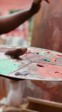 Dikey Video Özgüven Ressamı palette farklı suluboyaları karıştırarak mükemmel gölgeyi yaratıyor ve güzel sanatlara, tuvale uyguluyor. Sanatçı canlı renkler ve dinamik fırça darbeleri kullanır. Kapat.