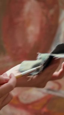Farklı renkleri karıştırmadan önce boya fırçasından boyayı silen dikey video kadın ressamı, boya tüpleriyle kırsal bir başyapıt yarattı. Sanatçı atölyede yeteneğini ve yaratıcılığını gösteriyor. Kapat