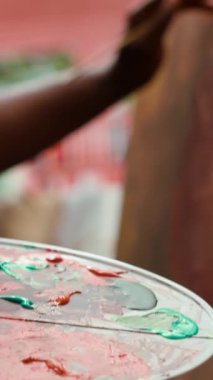 Dikey Video Özgüven Ressamı palette farklı suluboyaları karıştırarak mükemmel gölgeyi yaratıyor ve güzel sanatlara, tuvale uyguluyor. Sanatçı canlı renkler ve dinamik fırça darbeleri kullanır. Kapat.