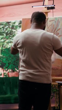 Dikey Video Ressamı, mükemmel gölgeyi yaratmak için bir palette birden fazla rengi karıştırıyor ve tuvalde güzel bir kırsal tablo yaratıyor. Erkek sanatçı, hobisi için sanatsal aletler ve malzemeler kullanıyor.