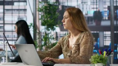 Kadın yönetici masasında iş operasyonlarını inceliyor, proje yönetimine odaklanmış. Çalışan, girişim stratejisini optimize etmek için performans ölçümlerini ve bütçe tahsislerini analiz eder. Kamera A.