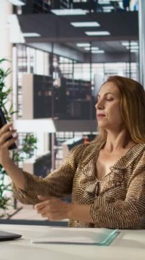 Dikey video özgüvenli genel müdür onun kurumsal çalışma yerinde gülümseyen ve fotoğraf çeken, resimlerle eğlenmek için cep telefonu kullanan. Akıllı telefondan selfie çeken gururlu bir girişimci. Kamera.