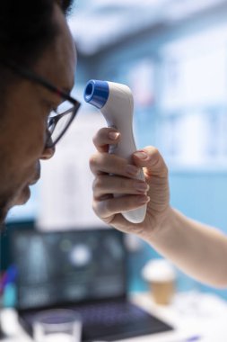 Sıcaklık ölçümlerini kontrol etmek için termometreyi kullanan bir sağlık uzmanı. Tıbbi konsültasyonda sıcaklık seviyelerini ölçüyor. Tanısal raporlar için dijital araç kullanan genç doktor.