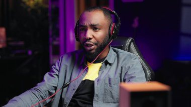 Bilgisayarda video oyunu oynayan, takım arkadaşlarıyla sohbet etmek için kulaklık takan bir adam. Oyuncu rakip oyuncularla çevrimiçi savaşıyor, kulaklıklar ve kamera A aracılığıyla iletişim kuruyor.