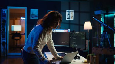 Bilgisayar bilimci evde yürüyor, dizüstü bilgisayar kullanarak yazılım uygulamaları geliştiriyor. IT uzmanı oturma odasında duruyor, şirket sistemlerini uyguluyor ve devam ettiriyor, kamera B