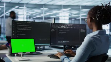 Bilgisayarlarda kod yazan ve ekipmanları güncelleyen bilişim destek çalışanları önünde izole edilmiş ekran tableti. PC masasındaki mühendisler sunucu kümelerini krom anahtar aygıtı, kamera B kullanarak denetlerler.