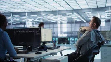 Monitördeki verileri analiz ederken kas kramplarını azaltmak için sunucu odasında esneme hareketleri yapmaktan yorgun düşmüş. Veri merkezindeki yorgun adam çok çalıştıktan sonra vücudu rahatlatıyor, kamera B