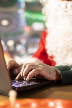 Noel Baba hediye takibi için internet sayfalarında gezinen şenlikli kütük kulübesinde bir laptop kullanıyor. Kuzey Kutbu Noel büyüsüyle dolu. Aziz Nicholas dijital çağı kucaklıyor..