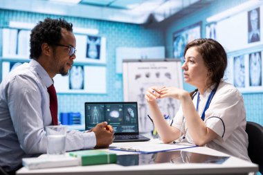 Muayene sırasında doğru teşhis için röntgen görüntülemesi sunan doktor, tıbbi konsültasyonda test sonuçlarını ve tedaviyi açıklıyor. Sağlık ekibi muayene sonuçlarını kabinede gösteriyor.