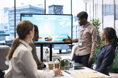 Üst düzey bir ofis alanında çalışan işçiler proje yönetimi görevlerinde işbirliği yaparak, iş akışı ve verimliliği artırmak için dijital araçlardan yararlanıyorlar. Etkileşimli panodaki büyük veriler gözden geçiriliyor.