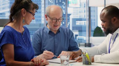 Komisyoncuyla emeklilik sözleşmesi şartlarını okuyan kıdemli kişiler, gelecek için mali yatırım sağlama seçeneklerini değerlendiriyorlar. Yaşlı çift uzmanla konuşuyor. Kamera A.