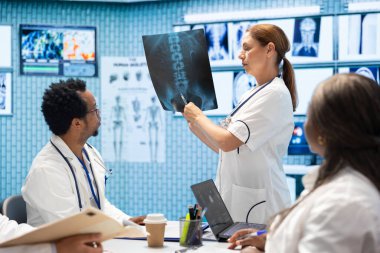 Doktor, bir toplantıda meslektaşlarına röntgen taraması sonuçlarını gösteriyor. Tanıya dayalı tedavi seçenekleri üzerinde uzmanlaşmış kişiler. Radyografi ile hastalıkları önleme stratejileri.