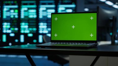 Yüksek teknoloji veri merkezindeki mühendislerin güvenlik tehditlerini izlemek için kullandıkları yeşil ekran laptopuna odaklan. Yönetmeliklere ve kamera A 'ya uyum sağlayan işçilerin kullandığı model defteri kapat.