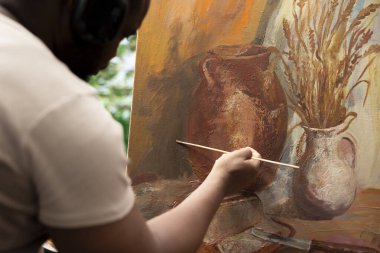 Kendine güvenen sanatçı tuvalin önünde duruyor suluboya resimlerle güzel bir tablo yapıyor, ince kıllar şeklinde. Fırça seti ve boya tüpleriyle renkli ve ilham verici bir sanat eseri yapmak. Kapat..