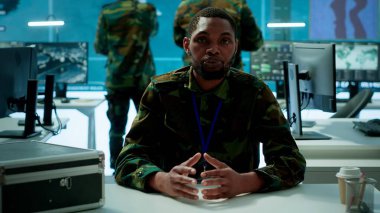 Askeri istihbarat uzmanı, iletişim ve karar verme işlemleri için birden fazla ekranda gerçek zamanlı verileri kullanarak modern bir komuta merkezinde stratejik bir telekonferans bağlantısı yürütüyor. Kamera A.