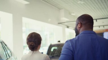Müşteriler araba galerisine geliyor, müşterilere uygun araçları sergilemeye hazır dost bir araba satıcısı tarafından karşılanıyorlar. Galeride yürüyen müşteriler, temsilci ve kamera B tarafından karşılanıyorlar.