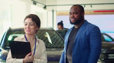 Galerideki müşteri araba satıcısıyla fiyat pazarlığı yapıyor. Afrika kökenli Amerikalı bir adam otomobil kiralamak için galeri acentasıyla görüşüyor. Araç kiralamayı umuyor. Kamera A