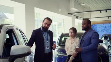 Galeri satıcısı araba kapısını açarak aracın markasını, modelini, kilometre oranını ve özelliklerini açıklıyor. Showroom temsilcisi müşterilerin potansiyel otomobilleri, kamera B 'yi değerlendirmesine yardımcı olur