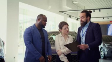 Müşterilerle buluşup ihtiyaçlarını tartışmak, satış tekliflerini desteklemek ve ilgili müşterilerle test sürüşlerine katılmak isteyen mutlu araba galerisi satıcılarının portresi, kamera B