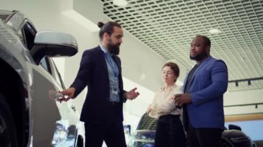 Araba satış temsilcisi müşterileri araç kapısına ve test kalitesine dokunmaya davet ederek bireylerin yatırım kararı almalarına yardımcı oluyor. Showroom temsilcisi müşterilerden otomobil özelliklerini kontrol etmelerini istiyor, kamera B