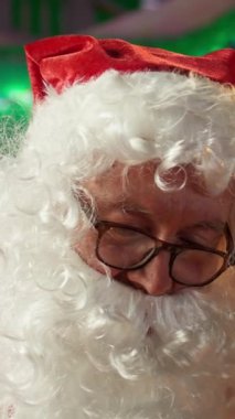 Dikey Video Aziz Nicholas atölyede şöminenin yanında bir hediye kutusu hazırlıyor. Kuzey Kutbu kulübesi Noel süsleri ve çocuklara hediyeler verme büyüsüyle dolu.