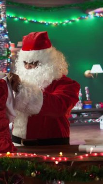 Dikey Video Afro-Amerikan Noel Baba 'nın hediyelerle dolu çantasını açması Noel ruhunun parlaması ve bayram neşesini yayması. Aziz Nicholas ağaç kulübesinde Noel 'in tadını çıkarıyor.