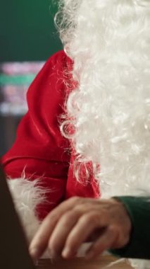 Dikey Noel Baba hediye takibi için internet sayfalarında gezinen şenlikli kütük kulübesinde dizüstü bilgisayar kullanıyor. Kuzey Kutbu Noel büyüsüyle dolu. Aziz Nicholas dijital çağı kucaklıyor.