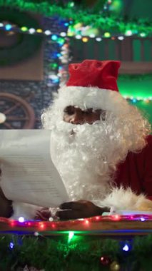 Dikey Video Siyah Noel Baba çocukların mektuplarıyla zarfları açıyor, Kuzey Kutbu 'ndaki şenlikli kulübede çocuklar için dilekleri yerine getiriyor. Noel neşesini yaymak için kış şenliği. Kamera B.