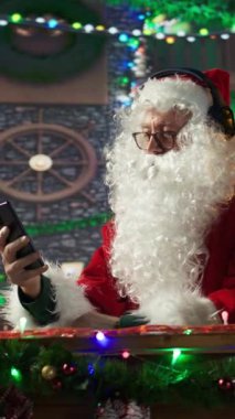 Dikey Videolu Neşeli Aziz Nicholas cep telefonundan Noel şarkıları dinliyordu. Beyaz sakallı adam, kış tatili ruhunu kulübesine yayıyordu. Dijital teknoloji