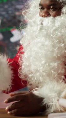 Dikey Video Baba Noel 'i, rahat festival atölyesindeki bir tabletten online hediye listesini kontrol ediyor. Kuzey Kutbu 'ndaki Afrikalı Amerikalı adam internet ve Noel büyüsüyle bağlandı. Kamera A.