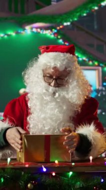 Dikey Noel Baba Noel Baba, Noel süslemeleriyle çevrili olan Kuzey Kutbu atölyesinde festival kağıdı ve kurdeleler kullanarak hediye kutusunu paketliyor. Noel Baba kış kutlaması için sürprizler hazırlar.