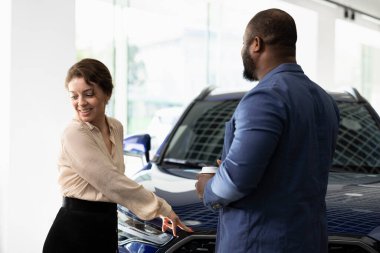 Gülümseyen karı-koca araba galerisinde tartışıyor, ödenecek bedelin ne olacağına karar veriyorlar, modelleri analiz ediyorlar. Galerideki kadın ve erkek araç satışından önce tartışıyor.