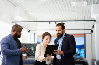 Araba galerisi satış yöneticileri müşterilerle ihtiyaçlarını tartışmak için toplanıyor. Aracın modellerini panoda sunuyorlar. Müşteriler galeri satıcısıyla sohbet ediyor. Onlara otomobilleri gösteriyor.