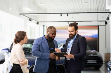 Araba galerisi satıcısı müşterilerle anlaştıktan sonra evrakları ve belgeleri tamamlıyor. Aracın anahtarlarını verdikten sonra müşterilerin imzalaması için satış sözleşmesi yapan ajan