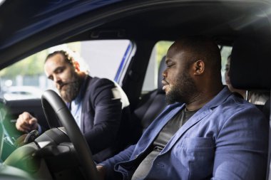 Deneme sürüşü sırasında araç özellikleri hakkında derin bilgi sağlayan satış danışmanı. Değerlendirmek için araba kullanan Afrikalı Amerikalı müşteri, galeri çalışanı ile konuşuyor.
