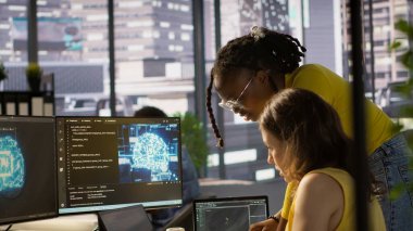 Büyük ölçekli makine öğrenme modellerini eğitmek için bulut hesaplama kaynaklarını kullanan iş arkadaşının yardımıyla. Kadın ve iş arkadaşı AI şirket sistemlerini bilgisayar, kamera A kullanarak izliyor.