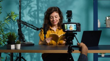 Excited content creator films video review of book, browsing through pages, impressed by story. Online star giving her impressions of new novel release to readers, giving positive feedback, camera A clipart