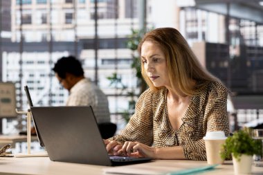 Kadın yönetici masasında iş operasyonlarını inceliyor, proje yönetimine odaklanmış. Çalışan, işletme stratejisini optimize etmek için performans ölçümlerini ve bütçe tahsisatlarını analiz eder.