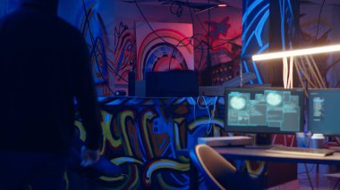 Hacker yeraltı üssüne geliyor, Grafiti çizimleriyle endüstriyel depodaki sprey kutulara bakıyor. Siber suçlu hackleme işlemini bekliyor, suç cennetindeki boya kutularına bakıyor, kamera B