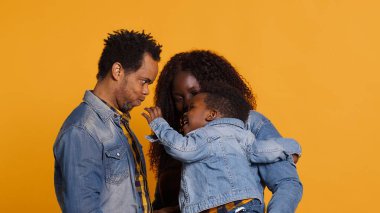 Afrikalı Amerikalı pozitif bir çift, küçük çocukları stüdyodayken birbirlerine sarılmış gülümseyen insanları dikizliyorlar. Mutlu sevgi dolu anne ve baba minnettarlık ve saygı gösteriyorlar. Kamera A.