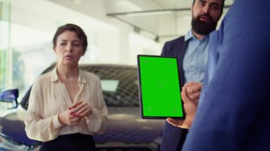 Satış elemanı müşterilerine yeşil ekran tabletinde araba modellerini gösteriyor, tavsiyelerde bulunuyor. Showroom temsilcisi, krom anahtar aygıtı B kamerasındaki müşterilere finansman seçenekleri sunar